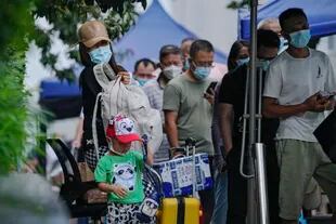 Una mujer y un niño con equipaje miran mientras residentes con mascarillas forman fila para recibir su prueba rutinaria de Covid-19 en Pekín el 3 de agosto del 2022. (AP Foto/Andy Wong)