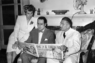 Juan Domingo Perón lee, junto a Eva y el coronel Domingo Mercante, un diario del día de la elección que cambiaría al país