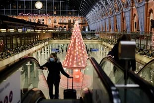 Un peatón que lleva un barbijo por la pandemia de Covid-19, viaja en una escalera mecánica cerca del árbol de Navidad "Tree of Hope", instalado dentro de la estación de tren St Pancras International en el centro de Londres, el 23 de noviembre de 2020