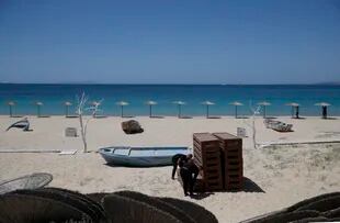 Trabajadores colocan tumbonas mientras otros instalan parasoles en la playa de Plaka, en la isla de Naxos, en el mar Egeo, el 12 de mayo de 2021. Grecia es uno de los países que forma parte del acuerdo del pasaporte sanitario