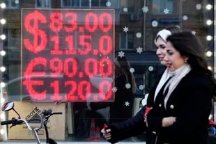 Due donne camminano davanti allo schermo di un ufficio di cambio che mostra i tassi di cambio del dollaro e dell'euro contro il rublo a Mosca. 