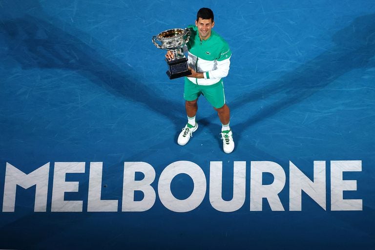 Novak Djokovic y el trofeo del Open australiano que alzó en 2021; el serbio busca festejar una vez más en Melbourne