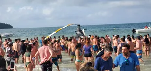 Turistas van a ver el helicóptero caído en la playa