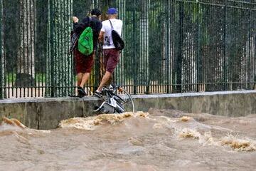  Los residentes caminan aferrándose a una cerca junto a una calle inundada durante las fuertes lluvias en Jardim Botanico