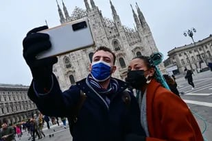 Una pareja de turistas se sacan una foto con sus barbijos frente al Duomo de Milán