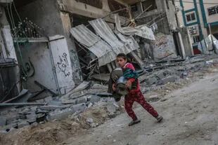 Una niña palestina lleva alguna de sus pertenencias que rescató de su casa  que fue alcanzada en un bombardeo