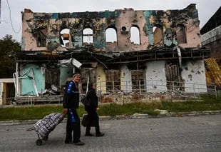 This photo taken on September 11, 2022 shows a couple carrying suitcases as they walk through a destroyed building in Izum, Kharkiv region of eastern Ukraine.