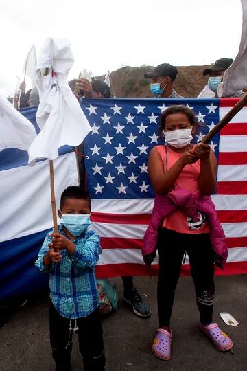 Los migrantes hondureños izan banderas blancas frente a una bandera hondureña y a una estadounidense, mientras los soldados y la policía guatemaltecos les impiden avanzar hacia la frontera con Estados Unidos