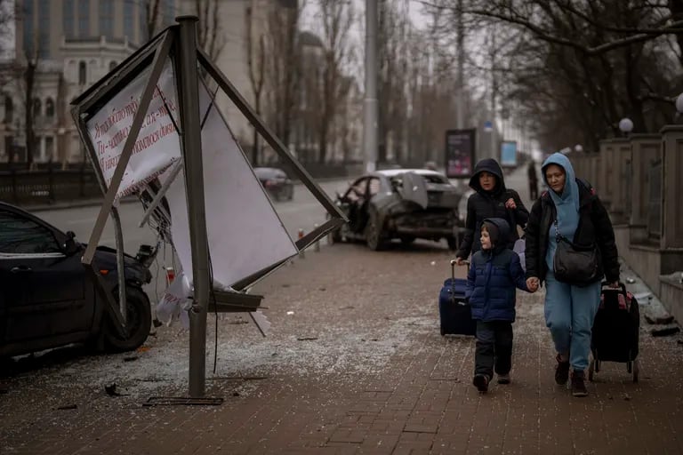 Dos mujeres y un chico caminan hacia la estación de tren de Kiev para escapar de la guerra en medio de los escombros