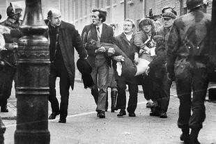 El cuerpo de Jackie llevado hacia afuera de la balacera; el padre Daily, a la izquierda de la imagen, llevaba un pañuelo blanco en la mano para abrirse paso entre la gente y los paracaidistas británicos