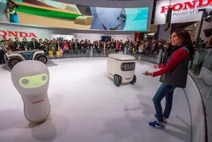 El stand de Honda con su robot de transporte (atrás a la izquierda), el de movilidad personal (el carrito junto a la presentadora) y 3E A18, el robot que intepreta emociones humanas
