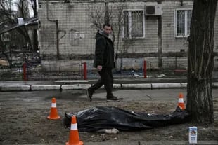 Un hombre pasa por delante de un cuerpo cubierto que yace en el exterior de un bloque de apartamentos destruido tras ser bombardeado en el distrito de Obolon, en el noroeste de Kiev, el 14 de marzo de 2022.