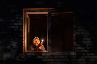 Una mujer alumbra con una vela desde su ventana ante los cortes de electricidad en Ucrania.