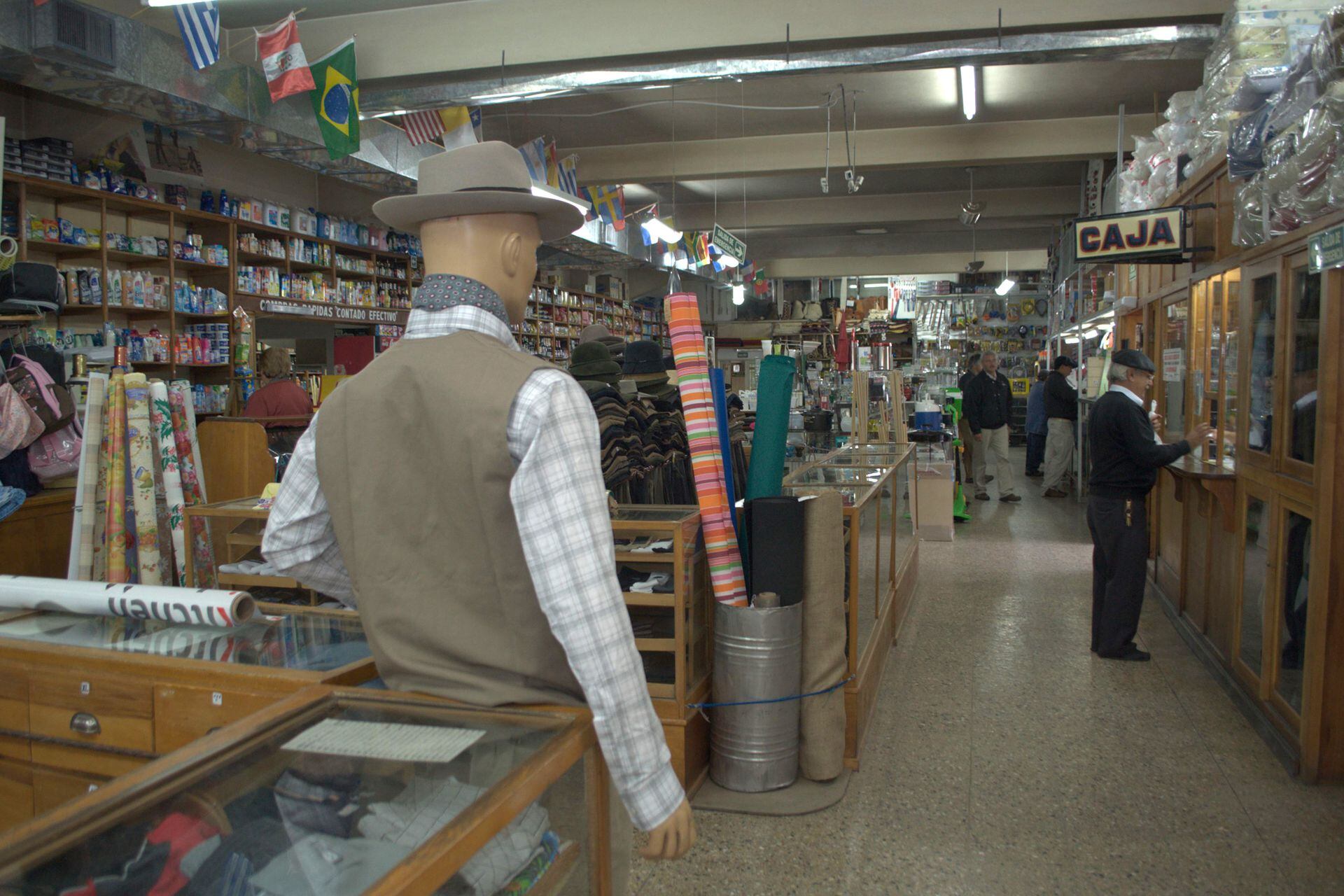 Maniquíes vestidos con sombrero entre los mostradores de madera maciza de las diferentes secciones del almacén.