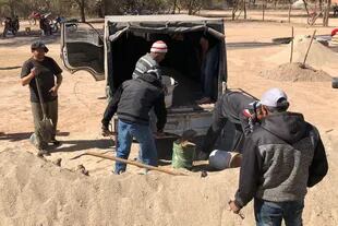 Algunos socios de la Asociación Civil de Pequeños Productores de La Candelaria cargan arena en un camión, otros arman rollos de alambre y los demás cargan bolsas de cal.