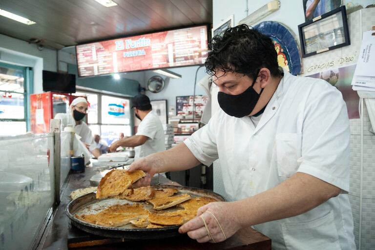 Víctor corta porciones de fainá en la pizzería El Fortín
