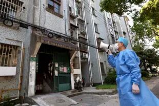 En esta foto publicada por la Agencia de Noticias Xinhua de China, un voluntario usa un megáfono para hablar con los residentes de un edificio de apartamentos en Shanghai, China