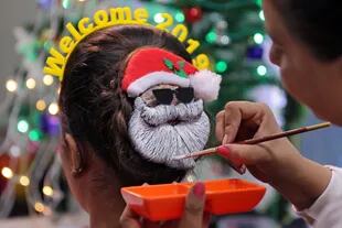 Una maquilladora pinta el pelo de una mujer en la forma de Santa Claus durante la celebración del año nuevo en Ahmedabad, India