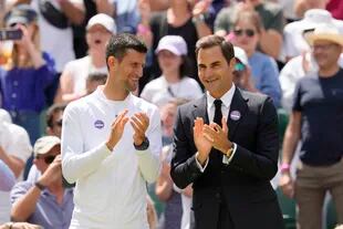 Novak Djokovic y Roger Federer aplauden durante el festejo del centenario de la Cancha Central de Wimbledon, el domingo 3 de julio de 2022. (AP Foto/Kirsty Wigglesworth)