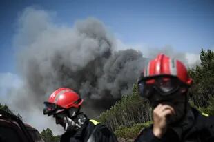 Firefighters stand on a road as heavy smoke is seen in the background during a forest fire near the town of Arigne, southwestern France on July 17, 2022.