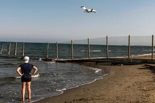 Un bañista se para en la orilla del mar mientras un jet hace su descenso hacia el Aeropuerto Internacional de Larnaca de Chipre el 1 de agosto de 2020