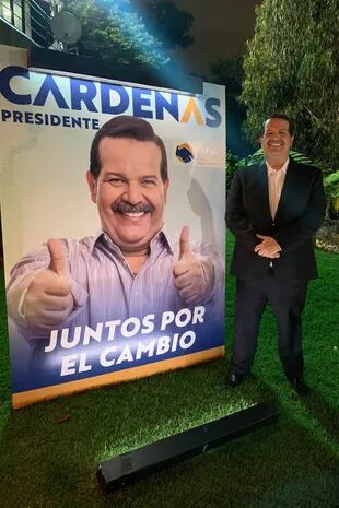 Mauricio Cujar, el actor que interpreta al candidato presidencial Braulio Cárdenas en Pálpito, sonríe frente al cartel de campaña de su personaje