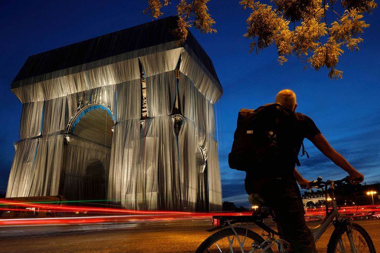 Un ciclista mira el Arco de Triunfo, en París, envuelto en una tela azul plateada como lo diseñó el difunto artista Christo, en la noche del 13 de septiembre de 2021