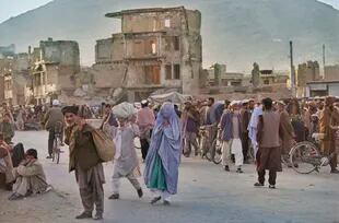 Una animada escena callejera con mujeres vestidas con niqab y hombres con turbantes afganos, con edificios dañados al fondo, Afganistán, 1996