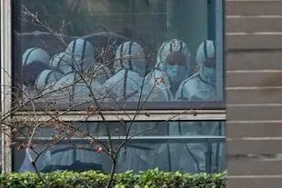 En esta imagen de archivo, miembros de un equipo de la OMS equipados con trajes de protección, vistos a través de una ventana durante una visita al Centro de Prevención y Control de Enfermedades de Animales, en Wuhan, en la provincia de Hubei, en el centro de China, durante una visita para tratar de descubrir los orígenes del coronavirus, el 2 de febrero de 2021