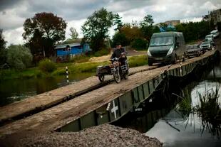 Lugareños y vehículos del ejército cruzan un puente temporal que sustituye a uno destruido en las cercanías, en Izium, Ucrania, el lunes 3 de octubre de 2022.
