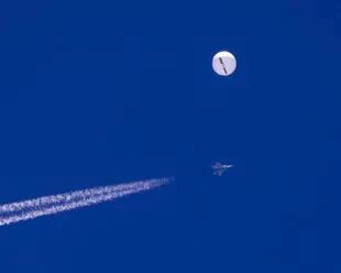 ARCHIVO - En esta foto provista por Chad Fish, un gran globo vuela sobre el Atlántico cerca de la costa de Carolina del Sur, y un avión de combate con su estela aparece por debajo, 4 de febrero de 2023. (Chad Fish via AP, File)