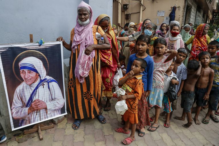 Personas sin hogar se reúnen junto a un retrato de Santa Teresa, la fundadora de las Misioneras de la Caridad, para reunir alimentos gratuitos afuera de la sede de la orden en Calcuta, India, el 26 de agosto de 2021. 