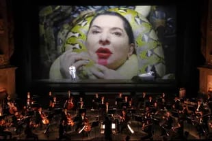 Marina Abramovic, en la cama, durante una escena de "Las siete muertes de Maria Callas", que se estrenó en 2021 en Munich. En la pantalla, cuando W. Dafoe le rodea el cuello con víboras para estrangularla como Desdémona, los serpenteantes animales se manchan con el lápiz labial de su cara