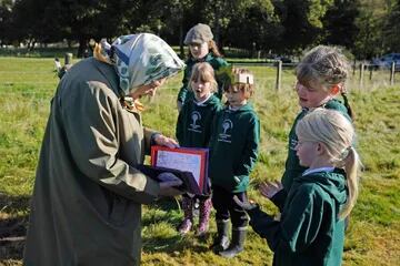 Los niños de la escuela primaria Crathie le presentan a la reina Isabel II de Gran Bretaña una tarjeta después de que la reina y el príncipe Carlos plantaron un árbol para marcar el inicio de la temporada oficial de plantación del Queen's Green Canopy (QGC), en el Balmoral Cricket Pavilion , Balmoral Estate en Escocia, el 1º de octubre de 2021