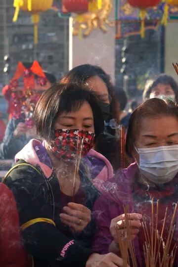 Fieles con máscaras faciales para protegerse contra la propagación del coronavirus, queman varitas de incienso mientras rezan en el Templo Wong Tai Sin, en Hong Kong