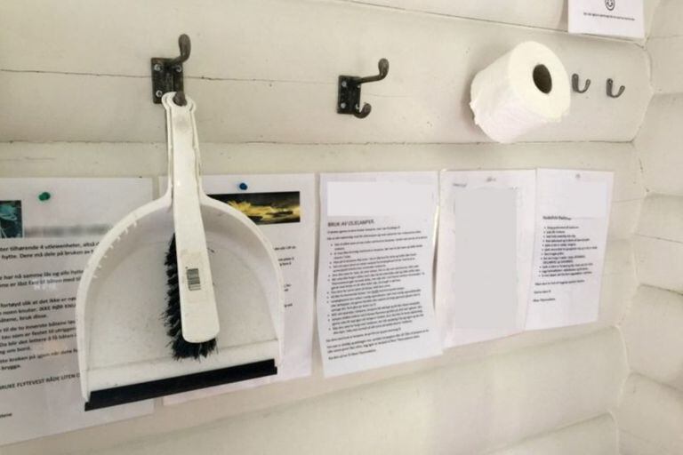 Un rollo de papel higiénico cuelga de la pared junto a un recogedor y un cepillo para usar en el baño exterior