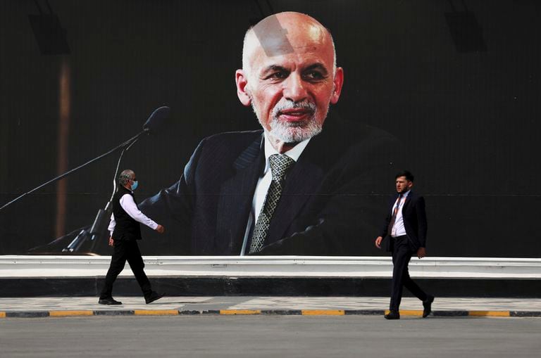 La gente camina cerca de un mural del presidente Ashraf Ghani en el aeropuerto internacional Hamid Karzai, en Kabul, Afganistán, el sábado 14 de agosto de 2021