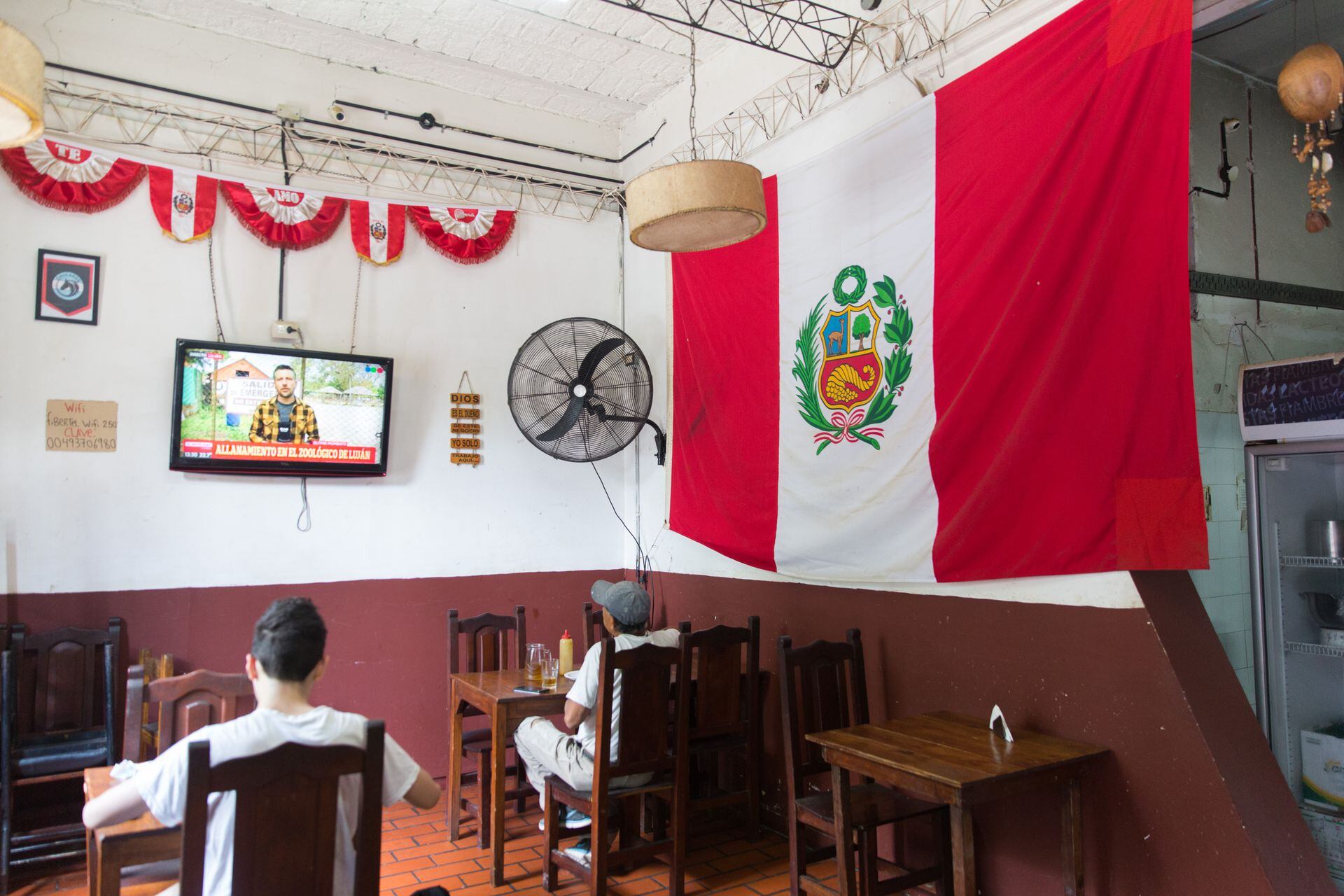 La bandera peruana cuelga de una de las paredes del salón, con la tele prendida.