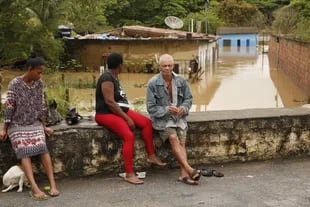 Personas esperan a que baje el nivel del agua de una calle afectada por la inundación provocada por la fuerte lluvia, en Itapetinga, estado de Bahía, Brasil, el 26 de diciembre de 2021.