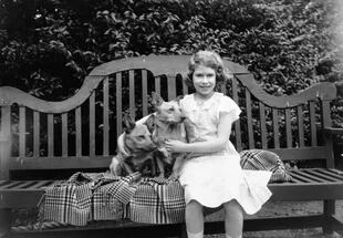 La princesa Isabel sentada en un asiento de jardín con dos perros corgi en su casa en 145 Piccadilly, Londres, en julio de 1936