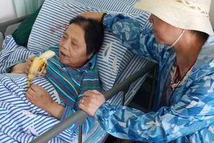 En esta fotografía proporcionada por su familia, Shen Peiming, de 71 años, come un plátano mientras miembros de su familia la cuidan en el Hospital Geriátrico Donghai, el 24 de septiembre de 2019, en Shanghái, China. (Familia de Shen Peiming vía AP)