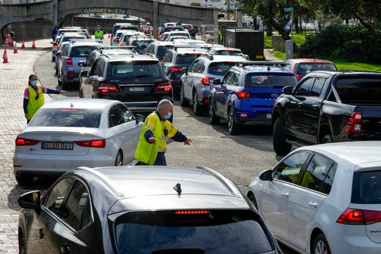 Le persone dirigono il traffico vicino a un centro di test diagnostici COVID-19 dove gli automobilisti non devono scendere dalle loro auto per sottoporsi al test, sabato 8 gennaio 2022, a Bondi Beach, Sydney, Australia.  (Foto AP/Mark Baker)