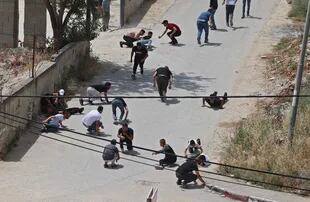 Palestinos se ponen a cubierto durante los enfrentamientos con las fuerzas de seguridad israelíes en la ciudad cisjordana de Yenín, el 13 de mayo de 2022. 