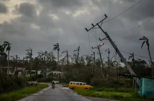 Un auto clásico estadounidense pasa junto a postes eléctricos inclinados por el huracán Ian en Pinar del Río, Cuba, el martes 27 de septiembre de 2022. (AP Foto/Ramón Espinosa)