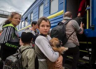 Un niño sostiene a su perro mientras su familia abandona una zona afectada por la guerra y sube a un tren de evacuación en Pokrovsk, en el este de Ucrania, el sábado 25 de junio de 2022. (AP Foto/Efrem Lukatsky)