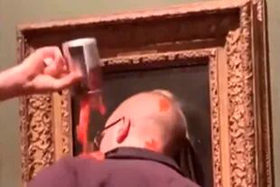 Detalle de uno de los activistas climáticos que intenta "pegar" su cabeza al cristal, que protege el cuadro de Vermeer, enchastrado con una "sustancia desconocida" que parece puré de tomate