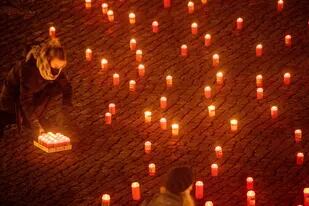 Gente encendiendo unas 1.500 velas en memoria de los fallecidos por el coronavirus en el nordeste de Alemania, en la plaza del mercado de Greifswald, Alemania, el lunes 17 de enero de 2022.  (Stefan Sauer/dpa via AP)