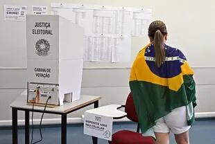 Una mujer envuelta en una bandera brasileña vota en un colegio electoral durante las elecciones legislativas y presidenciales, en Brasilia, Brasil, el 2 de octubre de 2022. (Foto por EVARISTO SA / AFP)