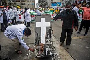 Trabajadores de la salud queman un ataúd simulado mientras protestan frente al Ministerio de Salud peruano exigiendo equipo de protección personal para manejar la nueva pandemia de coronavirus, en Lima, el 29 de septiembre de 2020