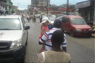 En en mercado central en Douala, junto a su hija en brazos, detrás un changarín lo secunda
